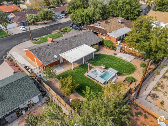 Aerial perspective of a fenced backyard featuring a covered patio, a manicured lawn, a built-in spa, and mature trees