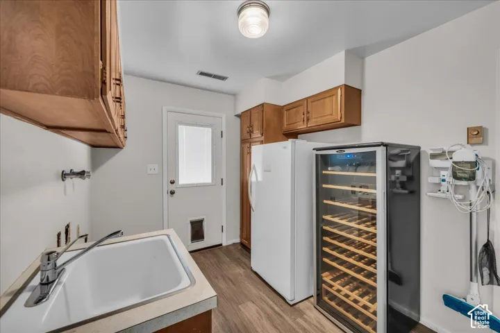 Utility area featuring wood-finish cabinetry, a drop-in sink with a high-arc faucet, wood-finish flooring, and a glass-paneled exterior door