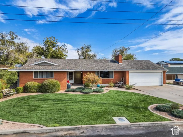 Single-story brick exterior featuring a multi-gable asphalt shingle roof, a prominent chimney, an attached two-car garage, and established front yard landscaping with curved concrete curbing
