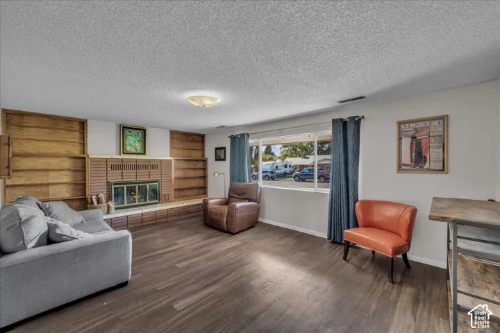 Living area featuring wood-finish flooring, a brick fireplace surround, and floor-to-ceiling built-in wooden shelving