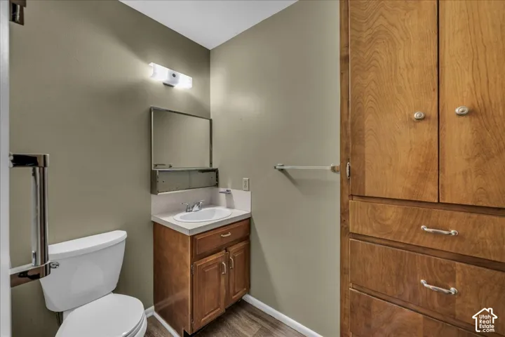 Built-in floor-to-ceiling wood cabinetry, wood-finish flooring, vanity with a solid surface countertop, rectangular mirror, and wall-mounted light fixture