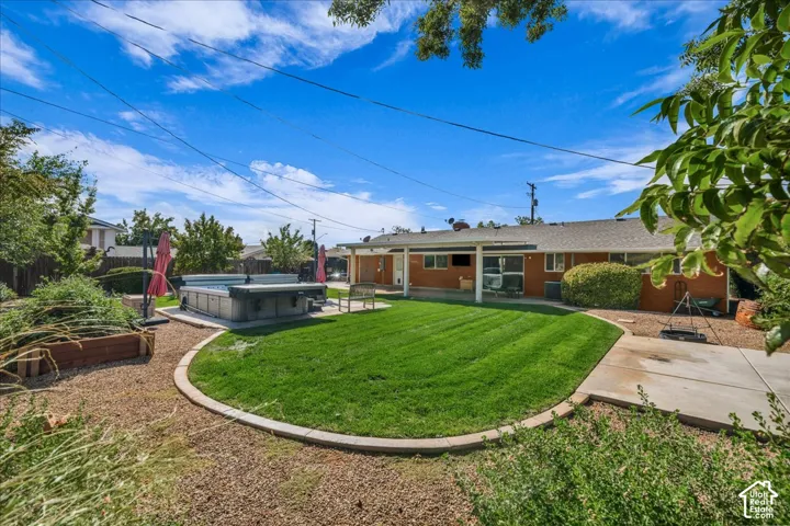 Backyard featuring a manicured lawn, concrete patio, raised garden bed with timber edging, built-in hot tub, and a covered patio area