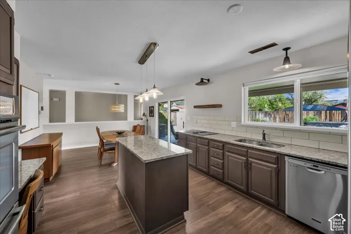 Kitchen featuring stone countertops, dark cabinetry, wood-finish flooring, subway tile backsplash, and a central island with pendant lighting