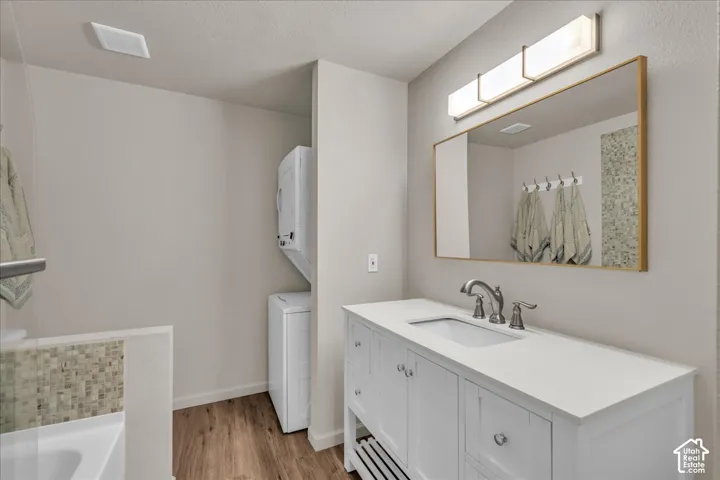 White vanity with integrated basin, solid-surface countertop, gold-tone framed mirror, linear vanity light, and wood-finish flooring