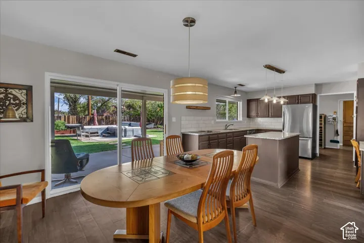 Kitchen featuring dark-finish cabinetry, an island with stone-surface countertop, subway tile backsplash, stainless steel refrigerator, and wood-finish flooring
