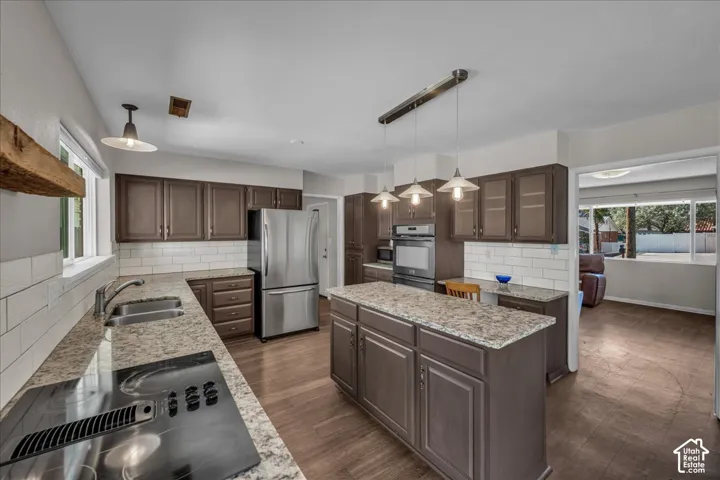 Kitchen featuring wood-finish flooring, stone-surface countertops, subway tile backsplash, built-in stainless steel appliances, and a central island