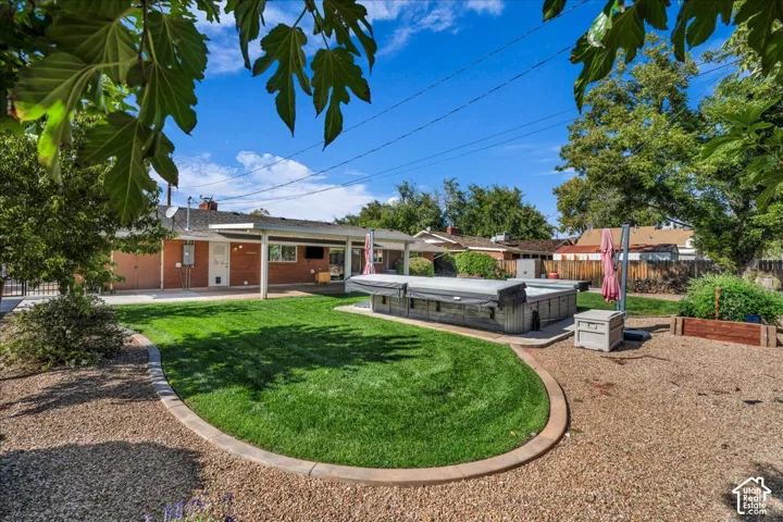Spacious backyard featuring a covered patio, a manicured lawn with curved concrete edging, a built-in spa with a cover, and raised garden beds