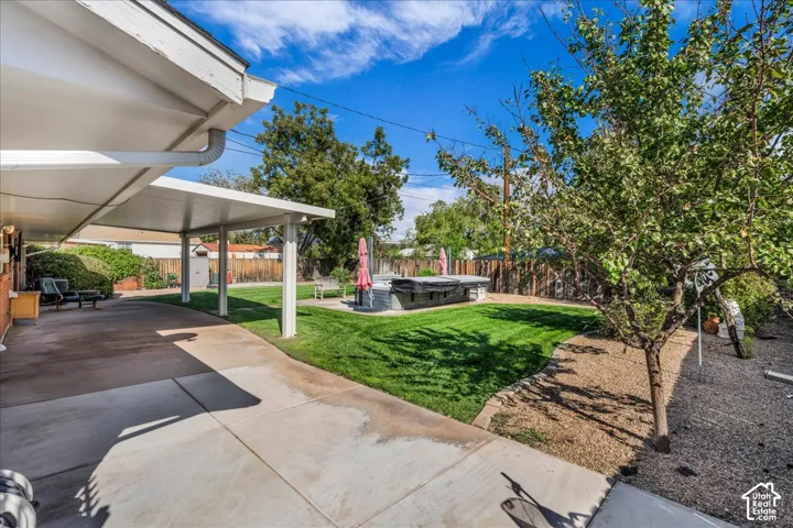 Covered concrete patio, expansive grass lawn, mature trees, and perimeter wood fencing