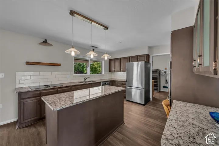 Kitchen featuring dark wood cabinetry, a central island, patterned stone-finish countertops, white subway tile backsplash, and stainless steel refrigerator