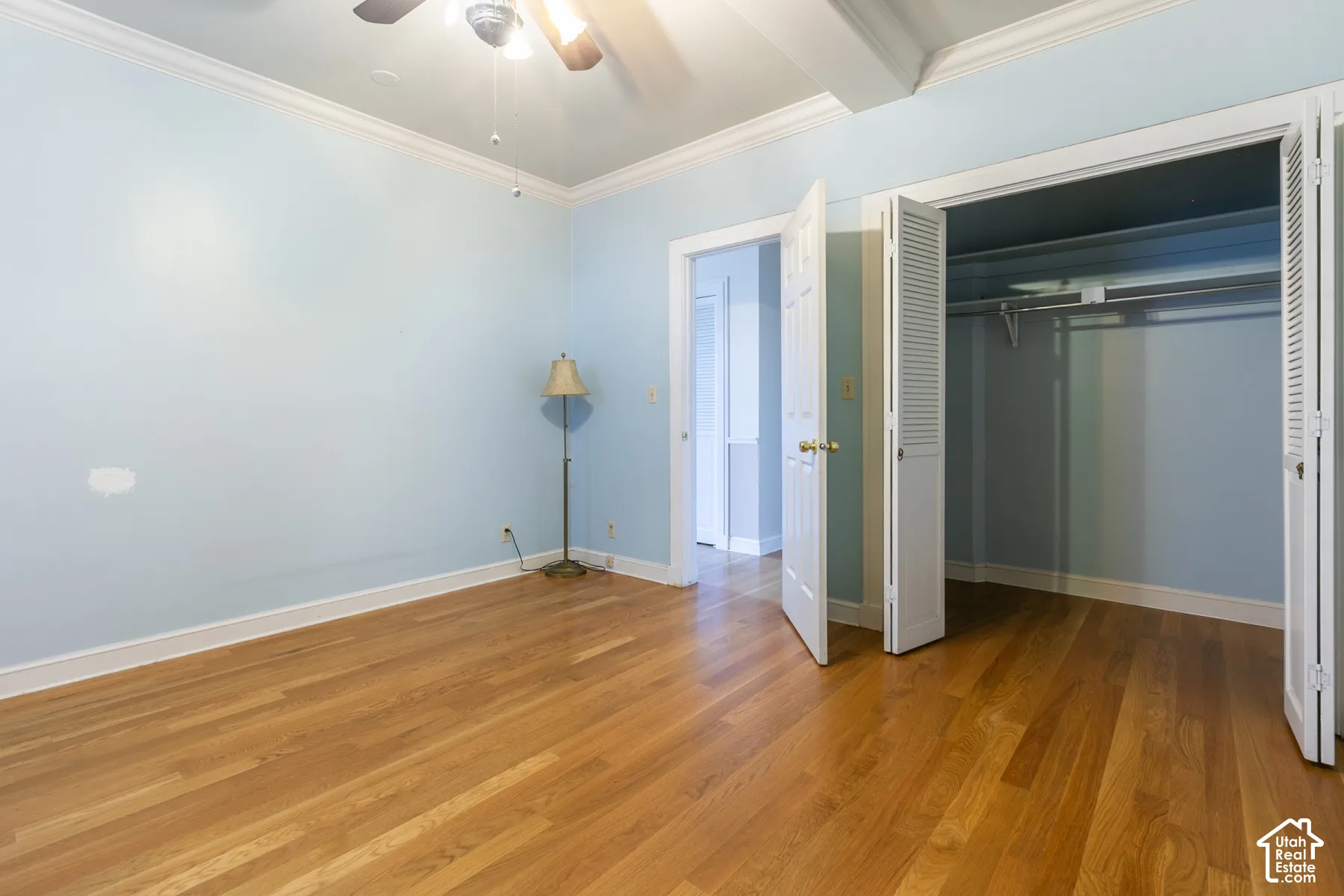 Room featuring wood-finish flooring, crown molding, a ceiling fan with integrated lighting, and a closet with bifold louvered doors