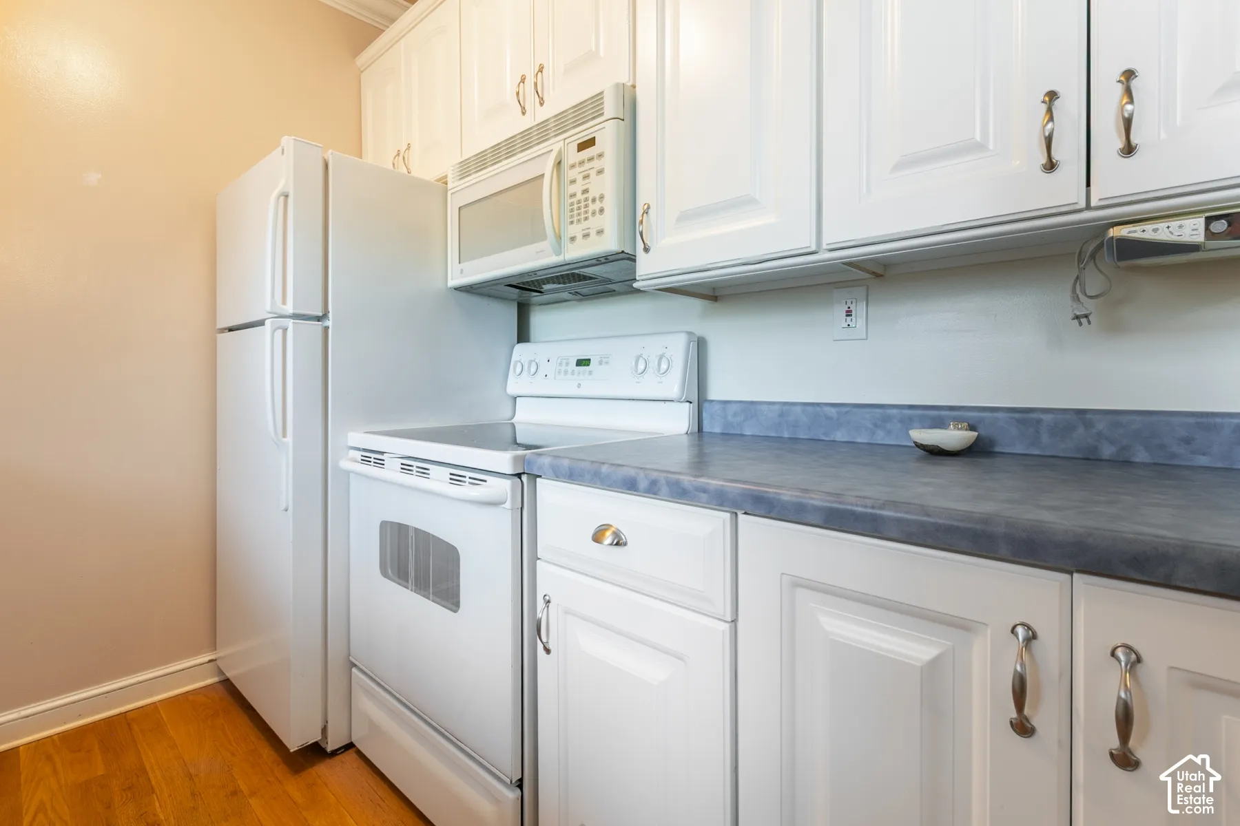 Kitchen featuring white cabinetry, wood-finish flooring, and white kitchen appliances including a range and over-the-range microwave
