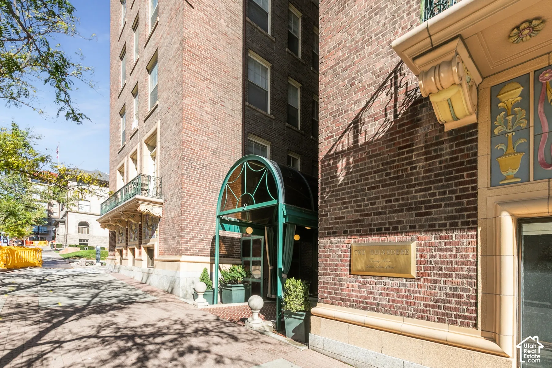 Multi-story brick exterior featuring a vaulted green metal canopy, decorative stone corbels, intricate masonry detailing, and a metallic building name plaque