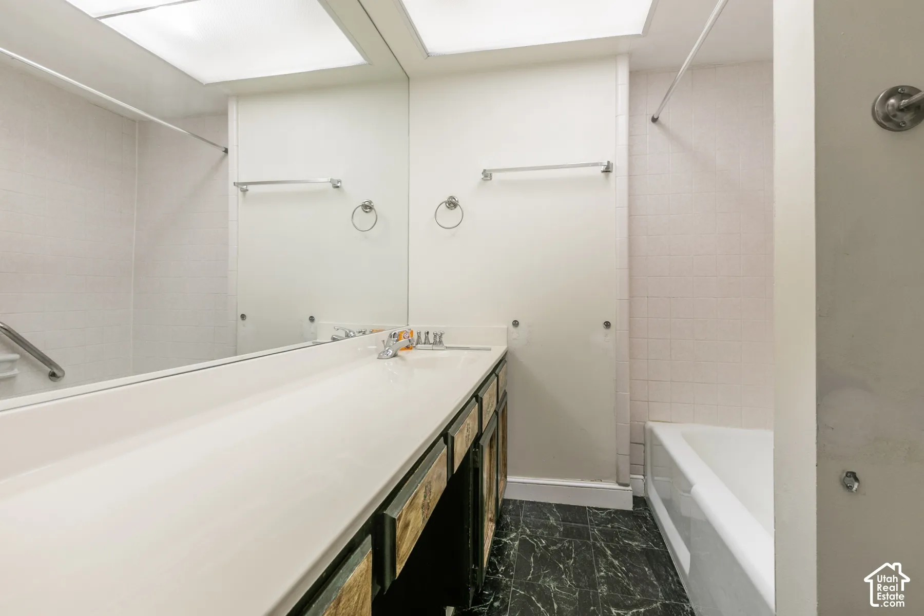 Bathroom featuring a full-width vanity with an expansive countertop, integrated sink, large wall-mounted mirror, and tile flooring