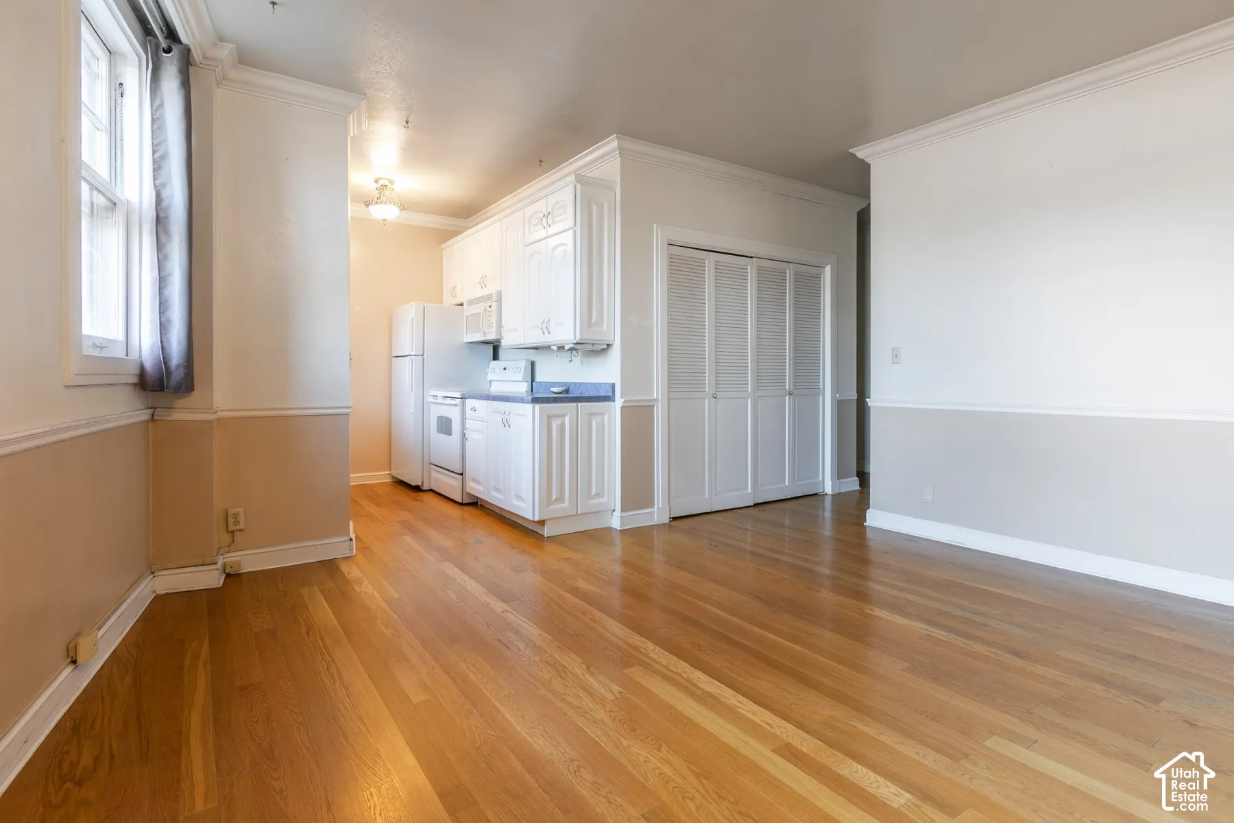 Wood-finish flooring throughout, white cabinetry with integrated appliances, louvered bi-fold closet doors, and crown molding