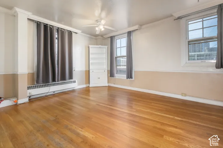 Wood-finish flooring, two-tone walls with crown molding, double-hung windows, built-in corner cabinet, and ceiling fan with integrated lighting