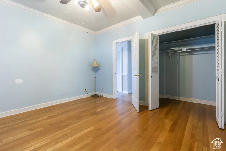 Room featuring wood-finish flooring, crown molding, a ceiling fan with integrated lighting, and a closet with bifold louvered doors