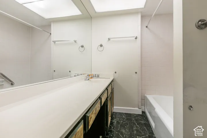Bathroom featuring a full-width vanity with an expansive countertop, integrated sink, large wall-mounted mirror, and tile flooring