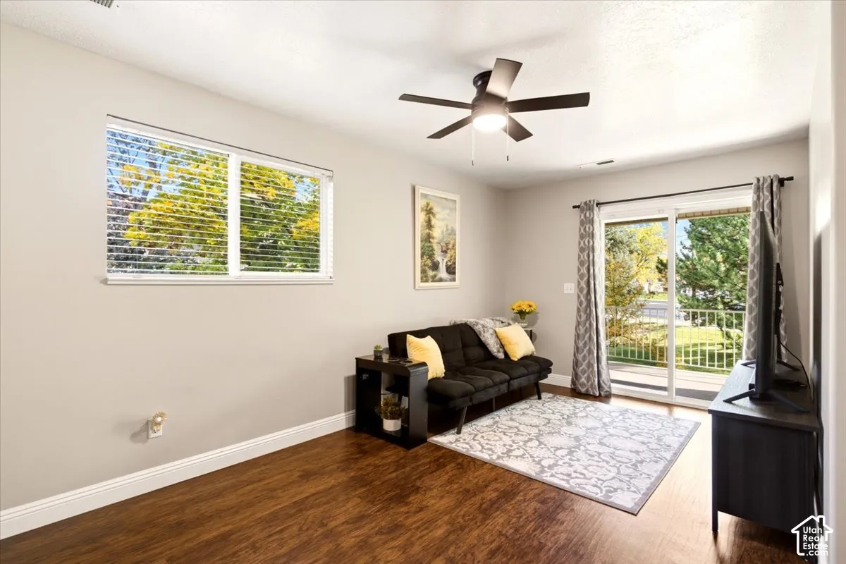 Wood-finish flooring, sliding glass door with balcony access, and a multi-blade ceiling fan with integrated lighting