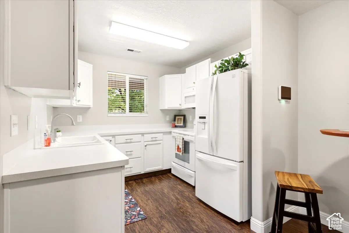 Kitchen featuring white cabinetry, solid-surface countertops, wood-finish flooring, integrated white appliances, and a single-basin sink