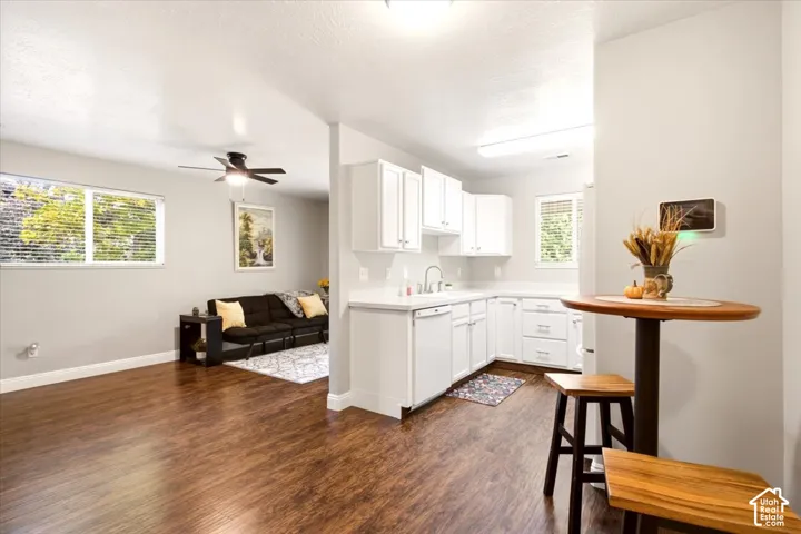 Kitchen featuring white shaker-style cabinetry, solid-surface countertops, and a built-in dishwasher, complemented by wood-finish flooring throughout the space