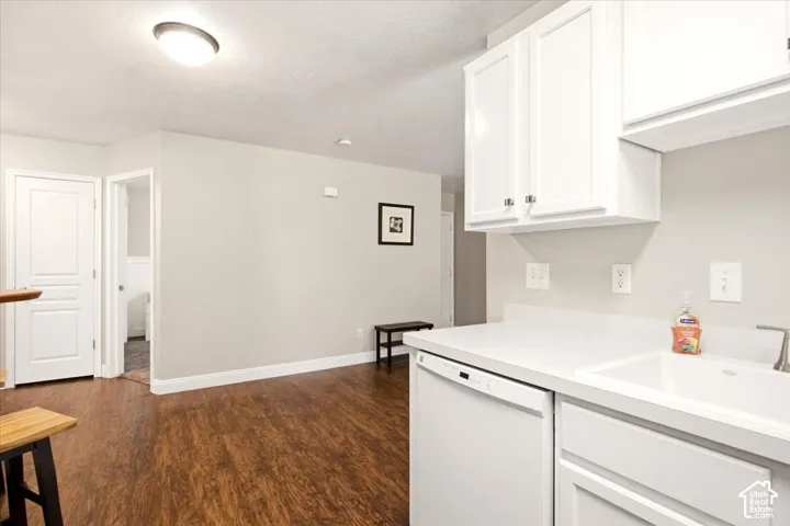 White cabinetry with shaker-style doors, integrated dishwasher, solid surface countertop, undermount sink, and wood-finish flooring