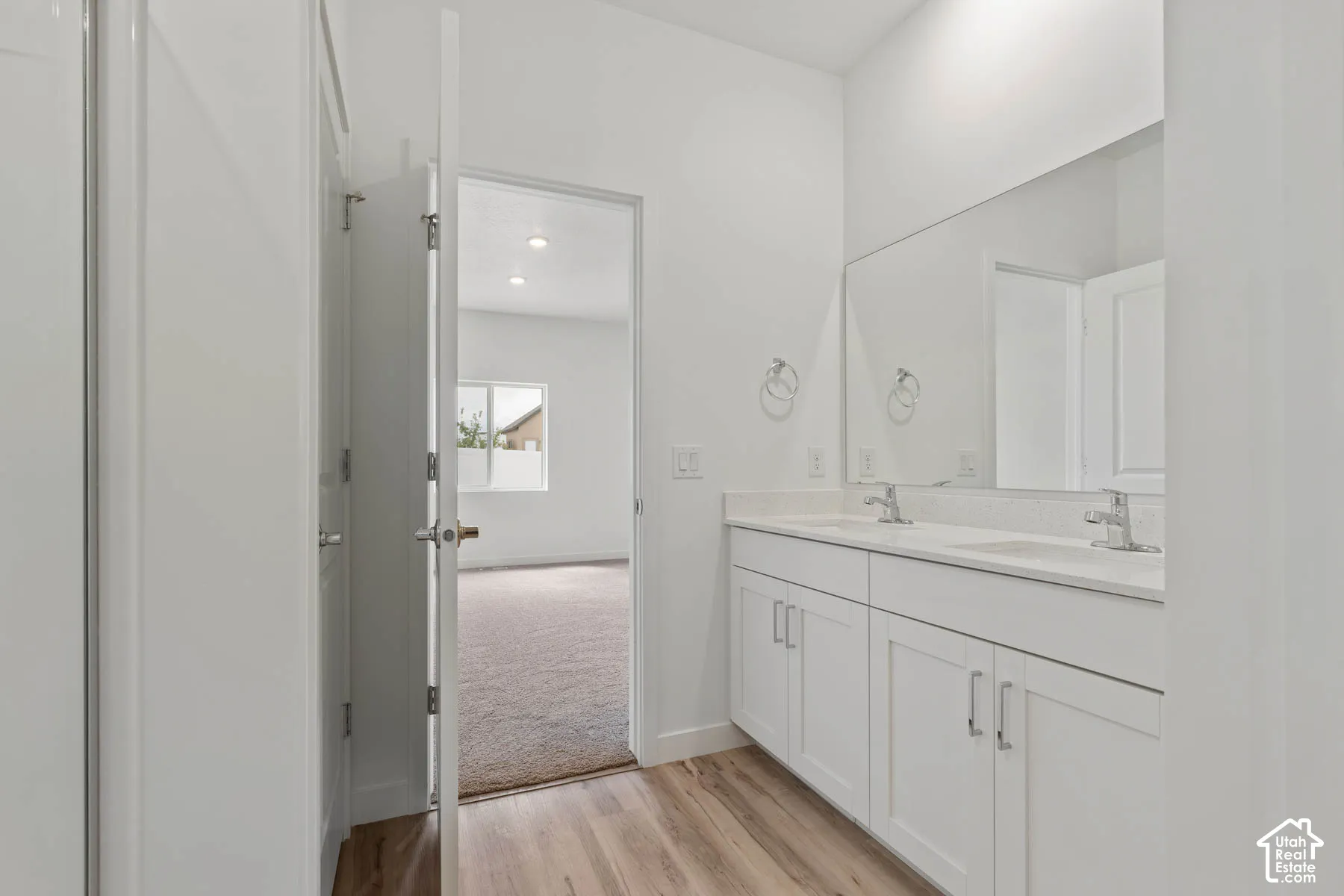 Double vanity featuring white cabinetry, light-toned stone-finish countertops, dual integrated sinks, and a full-width wall mirror