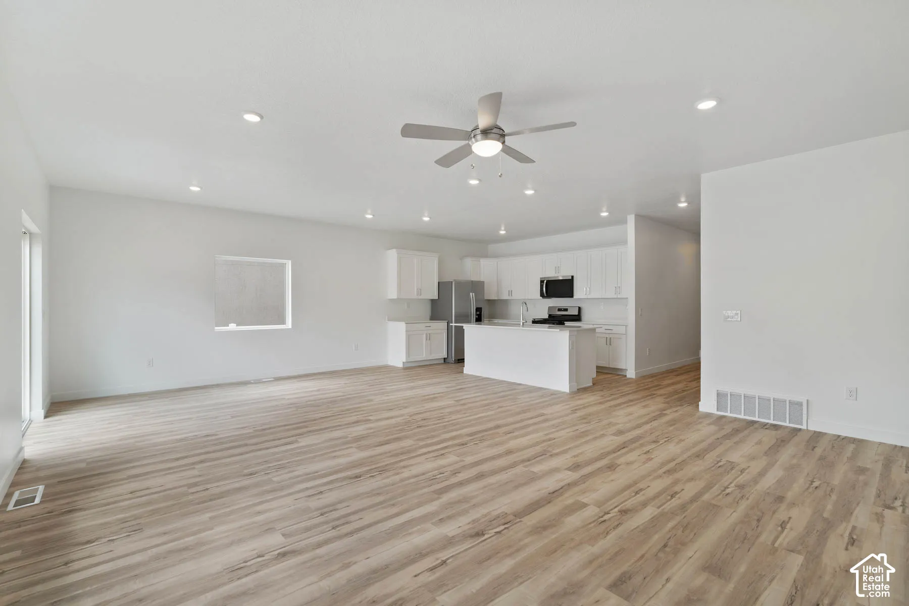 Open-concept interior featuring wood-finish flooring, recessed lighting, a central ceiling fan, white cabinetry, and a kitchen island