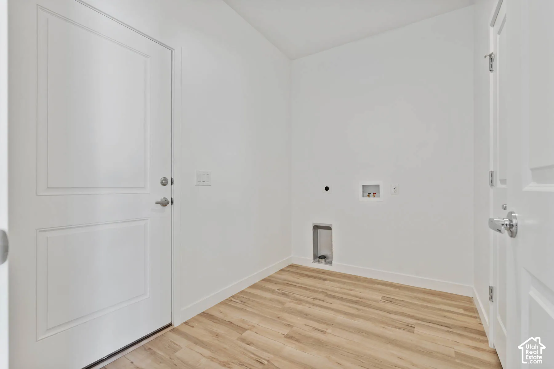 Utility room featuring wood-finish flooring, two panel-style doors with metallic hardware, and dedicated hookups for laundry appliances