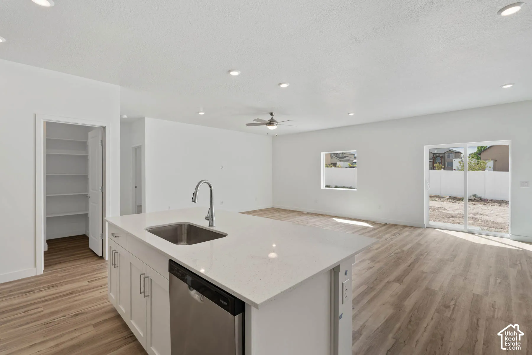 Kitchen island with white cabinetry, quartz countertop, stainless steel undermount sink, and integrated dishwasher