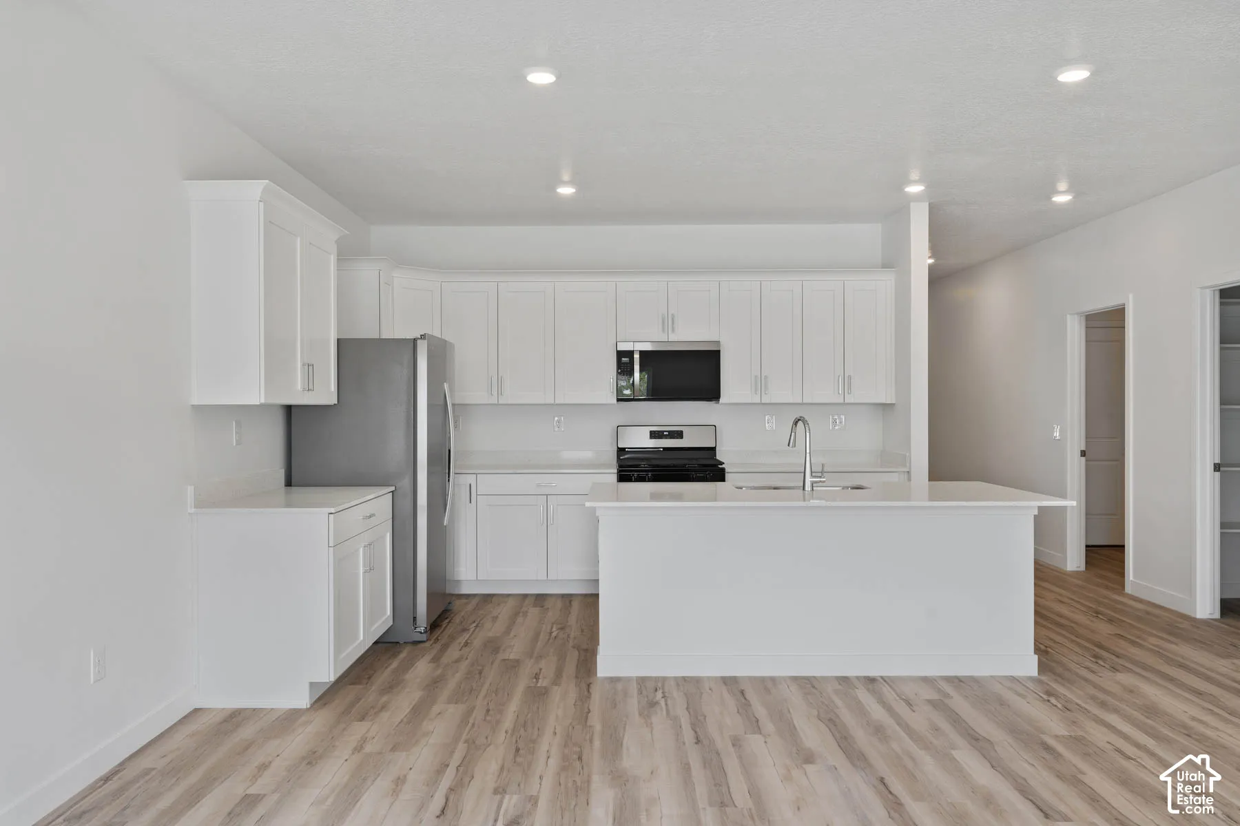 Kitchen featuring white shaker-style cabinetry, a central island with a sink, stone countertops, stainless steel appliances, and wood-finish flooring