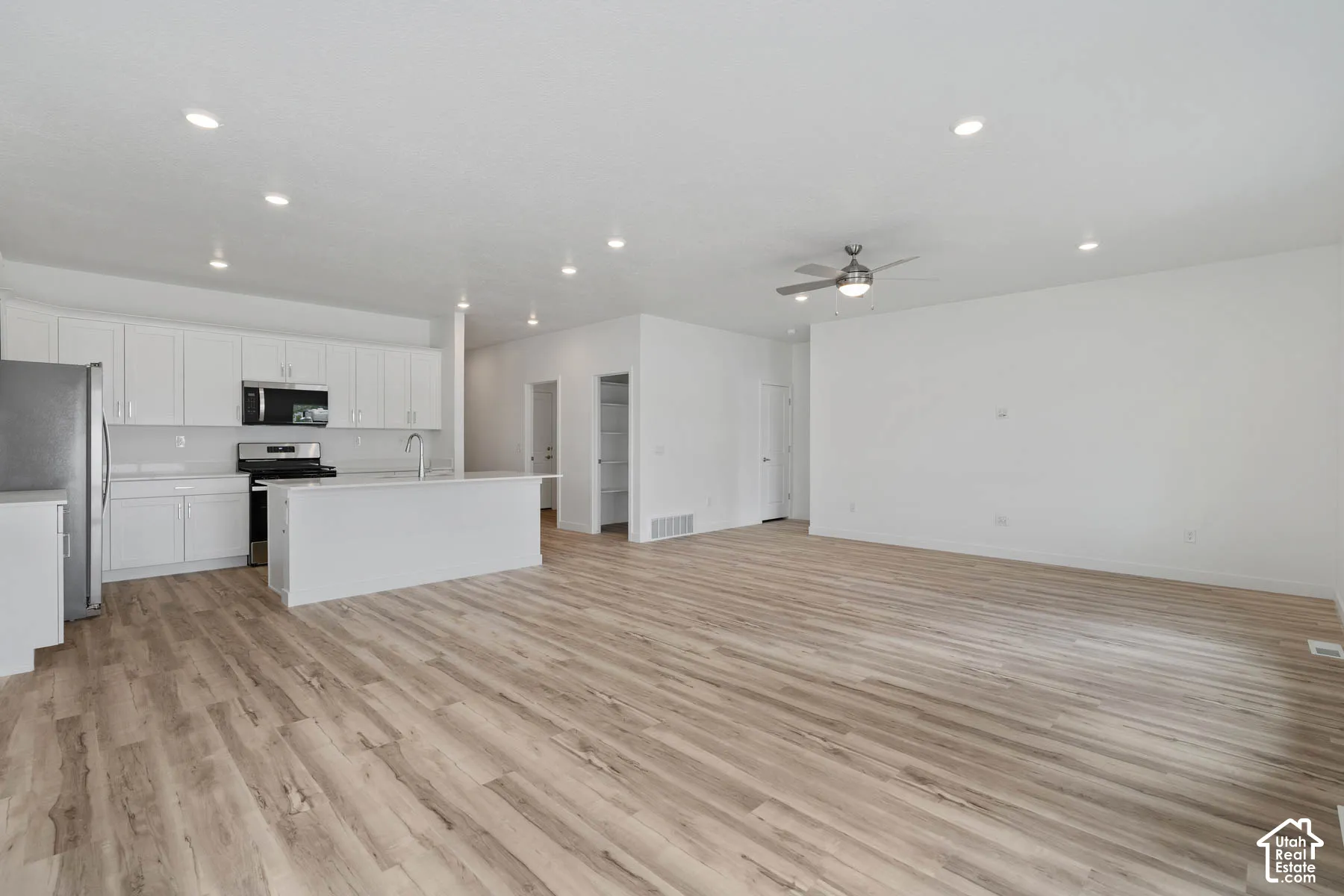 Kitchen featuring white cabinetry, an island with countertop, stainless steel appliances, wood-finish flooring, and recessed ceiling lighting