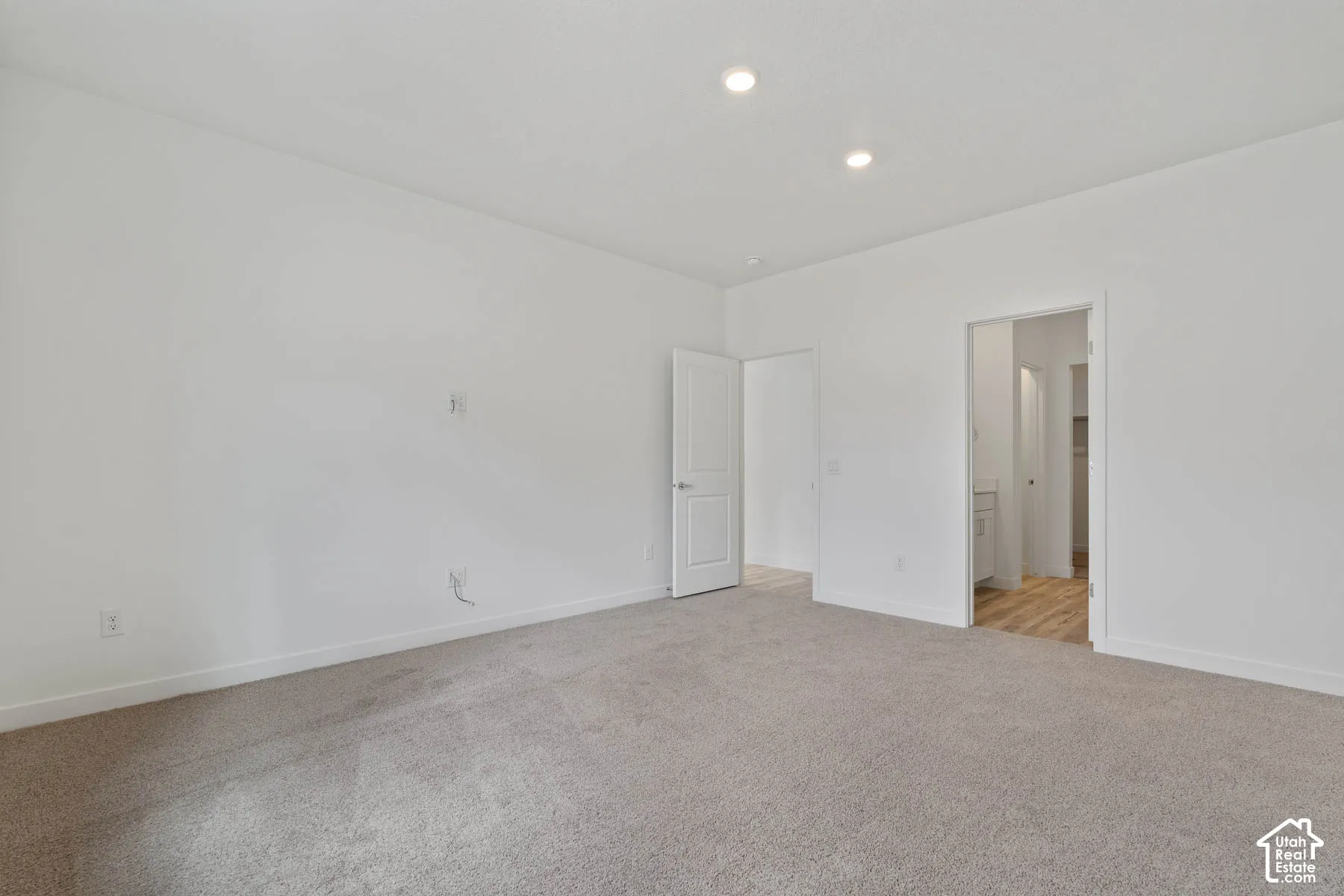 Interior space featuring neutral-toned carpeting, white walls, recessed ceiling lighting, and a multi-panel interior door
