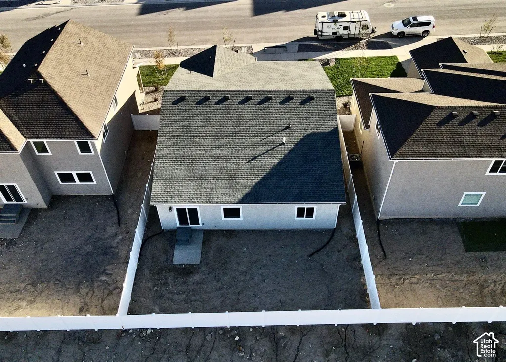 Rear exterior featuring a multi-pitched shingle roof, light-toned stucco siding, white vinyl privacy fencing, and a concrete patio