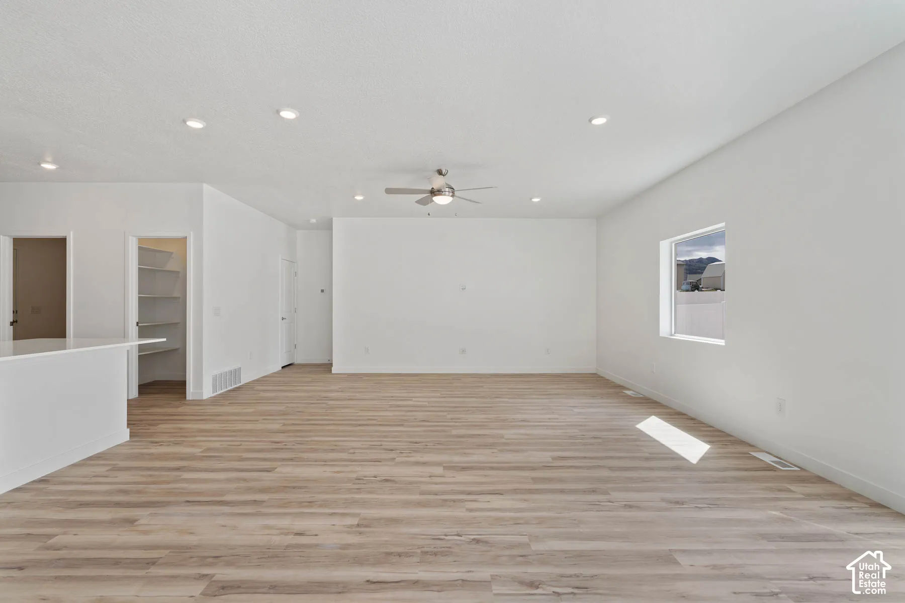 Open-concept interior featuring wood-finish flooring, recessed lighting, a ceiling fan, and an integrated pantry with built-in shelving