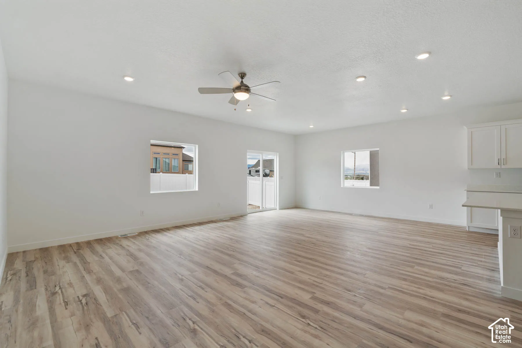 Open-concept interior featuring wood-finish flooring, recessed lighting, a ceiling fan, white cabinetry, and sliding glass doors
