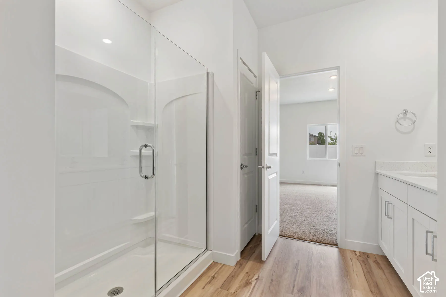 Bathroom featuring a walk-in shower with a glass enclosure, wood-finish flooring, white shaker-style vanity cabinetry, and a solid-surface countertop