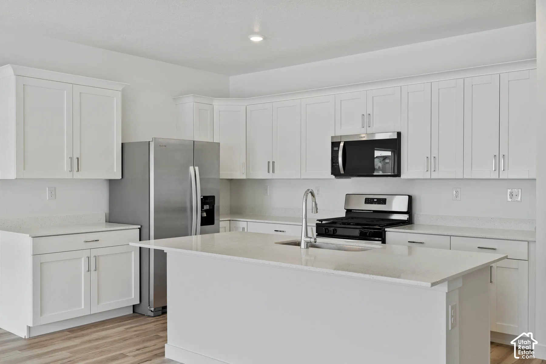 Kitchen featuring white shaker-style cabinetry, a central island with a quartz countertop, stainless steel appliances, and wood-finish flooring