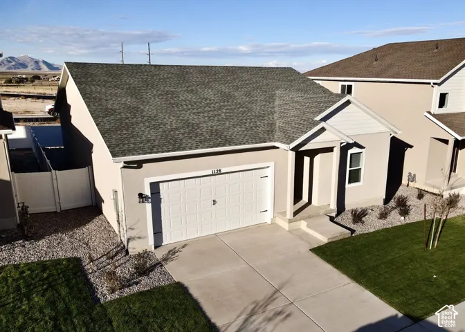 Single-story exterior featuring a stucco facade, an asphalt shingle roof, a two-car garage, and low-maintenance gravel landscaping