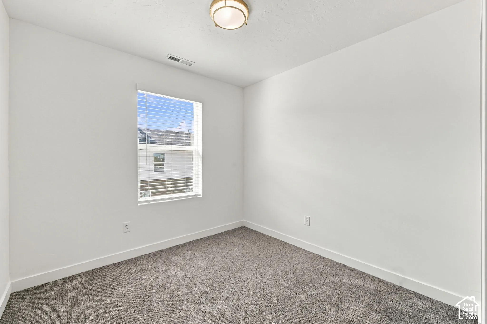 Neutral interior room featuring grey carpeting, crisp white walls, a single-pane window with white blinds, and a semi-flush mount ceiling light fixture
