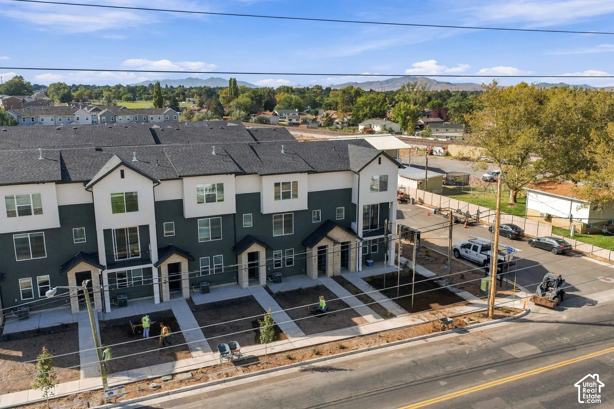 Multi-story residential complex featuring dark-toned siding with white trim, asphalt shingle roof, concrete walkways, and mountain backdrop