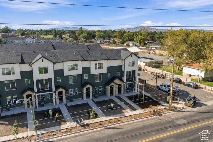 Multi-story residential complex featuring dark-toned siding with white trim, asphalt shingle roof, concrete walkways, and mountain backdrop