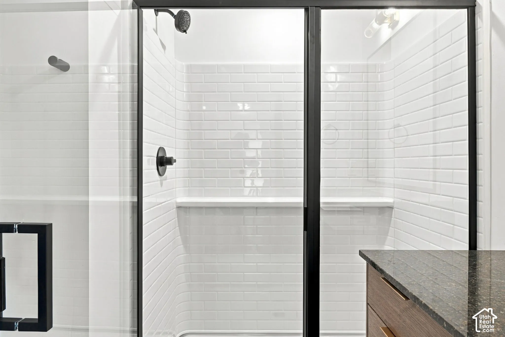 Walk-in shower featuring white subway tile, black-framed glass enclosure, matte black fixtures, and built-in shelving