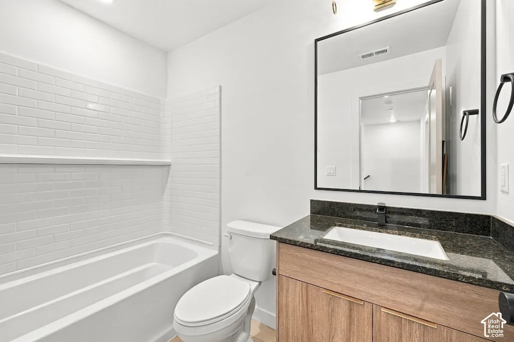 Bathroom featuring a vanity with a wood-finish cabinet, dark stone countertop, integrated rectangular sink, matte black faucet, and a subway-tiled tub surround