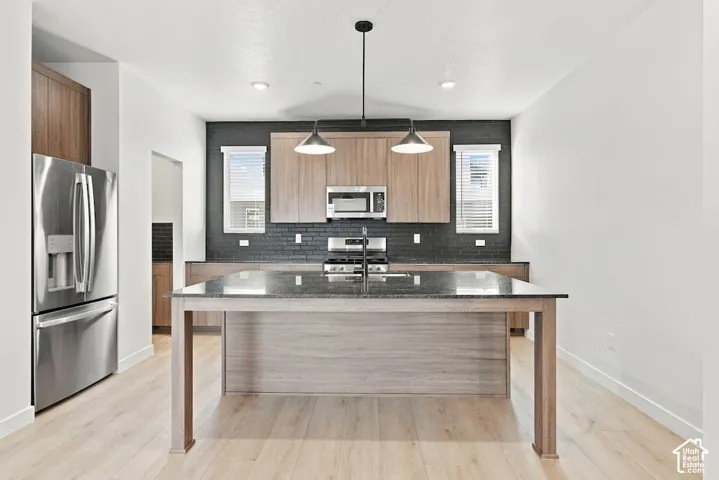 Kitchen featuring a central island with a stone countertop, flat-panel cabinetry, stainless steel appliances, dark tile backsplash, and wood-finish flooring