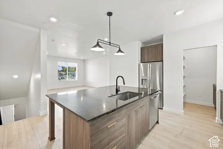 Kitchen featuring a central island with a dark stone countertop, integrated sink, matte black faucet, and wood-finish cabinetry