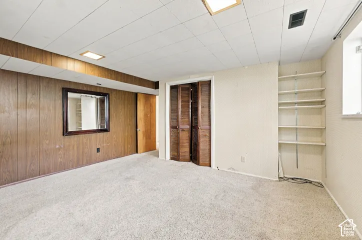 Interior room featuring wood-paneled wall accents, built-in shelving, carpeted flooring, and a folding wood-door closet
