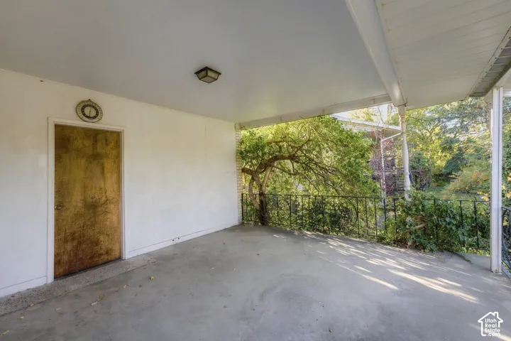 Covered exterior porch featuring a concrete floor, wrought iron railing, and a flush-mount ceiling light fixture