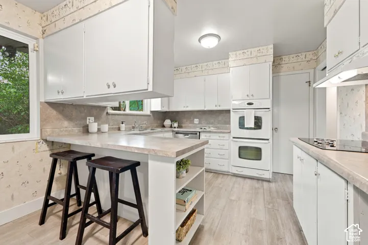 Kitchen featuring white cabinetry, integrated double wall ovens, built-in cooktop, laminate countertops, and wood-finish flooring