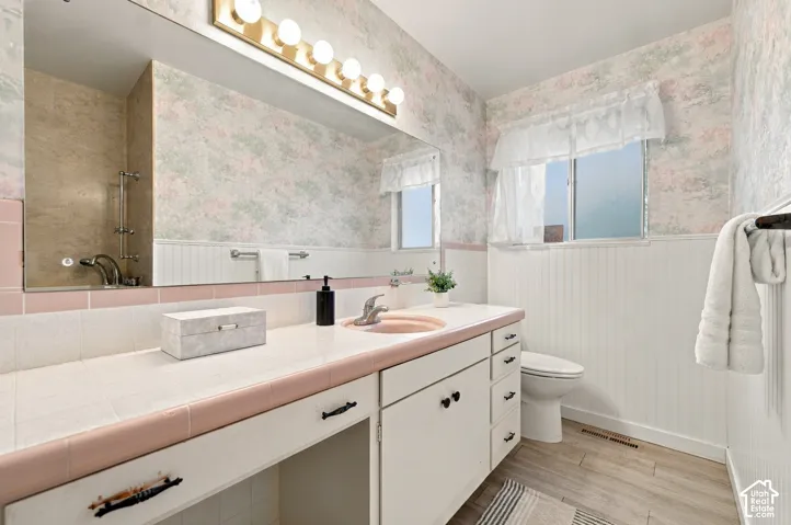 Bathroom featuring a tile-topped vanity with an integrated basin, white cabinetry, beadboard wall paneling, and a large-format vanity mirror with integrated lighting