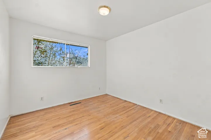 Room featuring wood-finish flooring, white walls, a single-pane sliding window, and a flush-mount light fixture